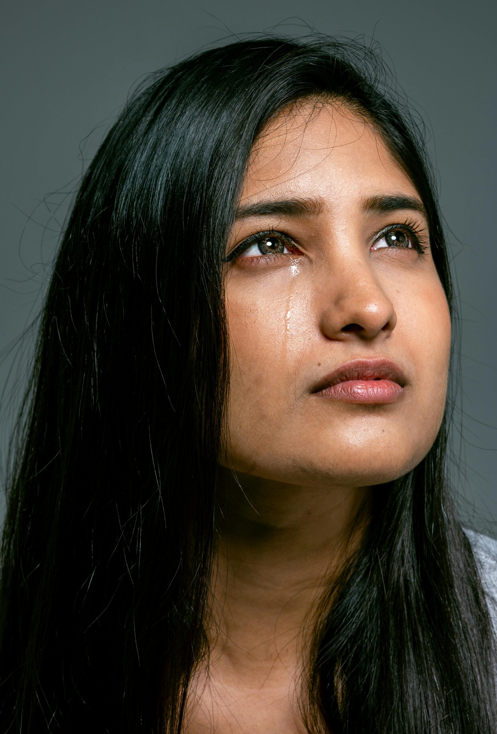 Close-up of a young woman in a studio setting expressing emotion with a tear.